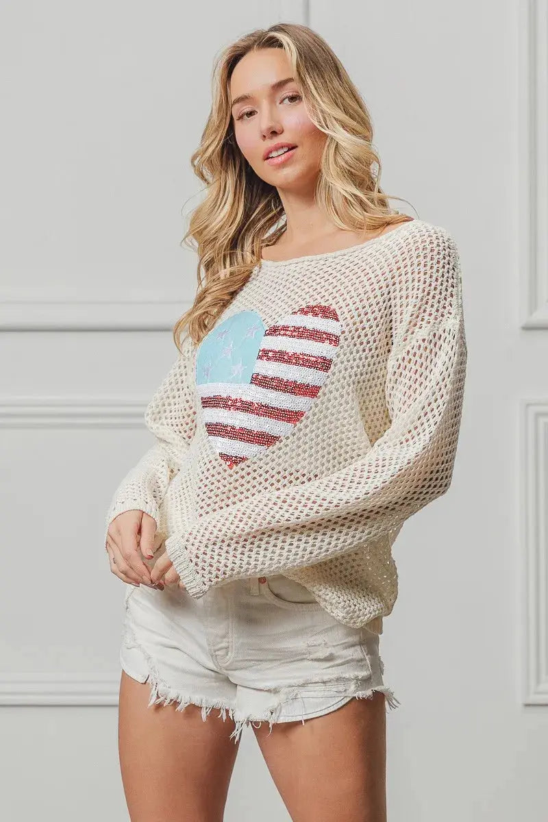 Woman wearing a mesh sweater with a heart design in front of a white wall.