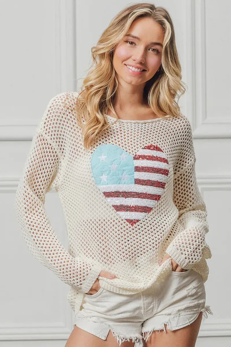 Woman wearing a cream sweater with a heart-shaped American flag design.