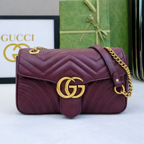 Maroon handbag with gold chain and Gucci logo in front of a Gucci branded box.