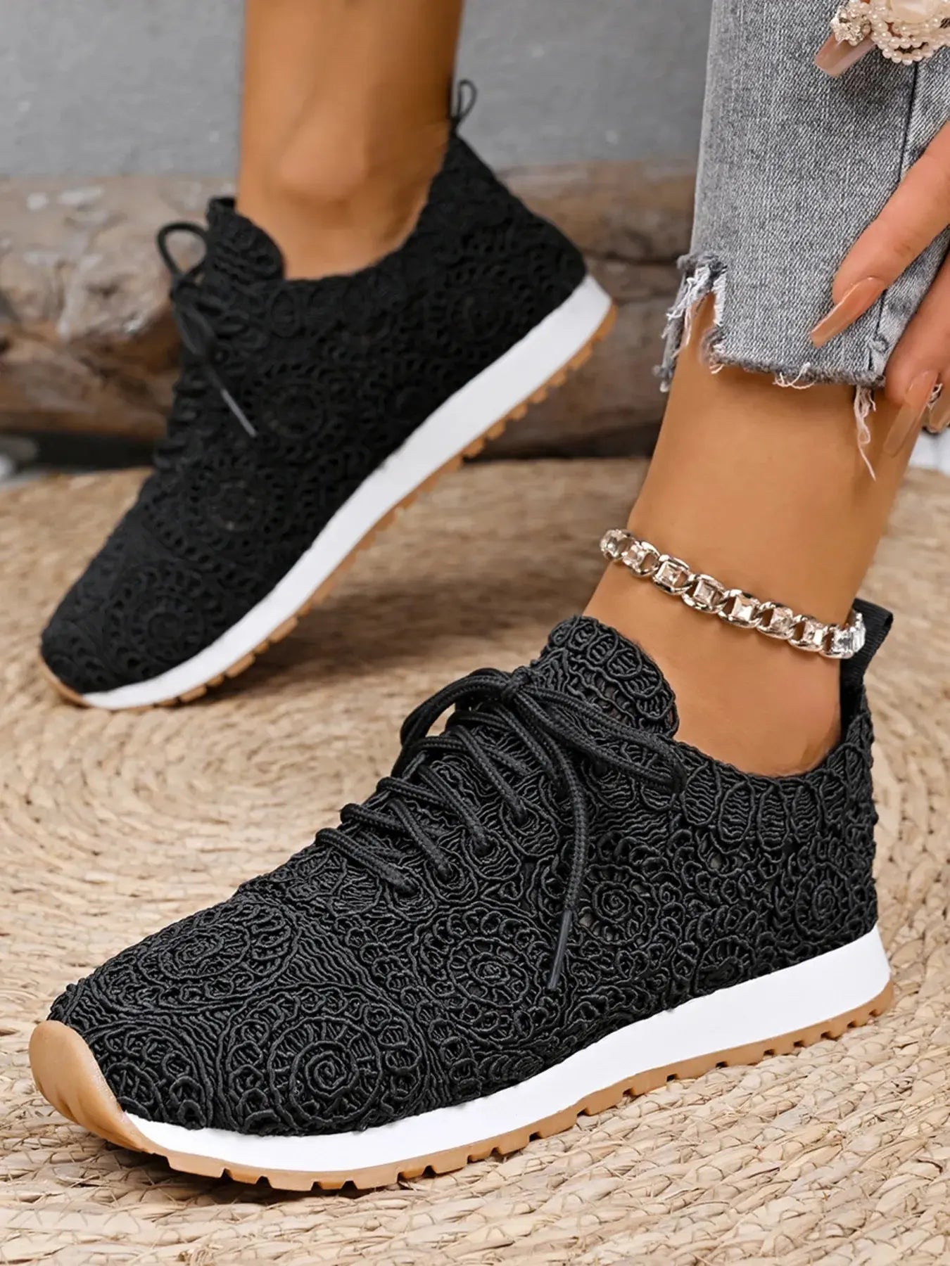 Black lace-up sneakers worn on a textured surface with a neutral background