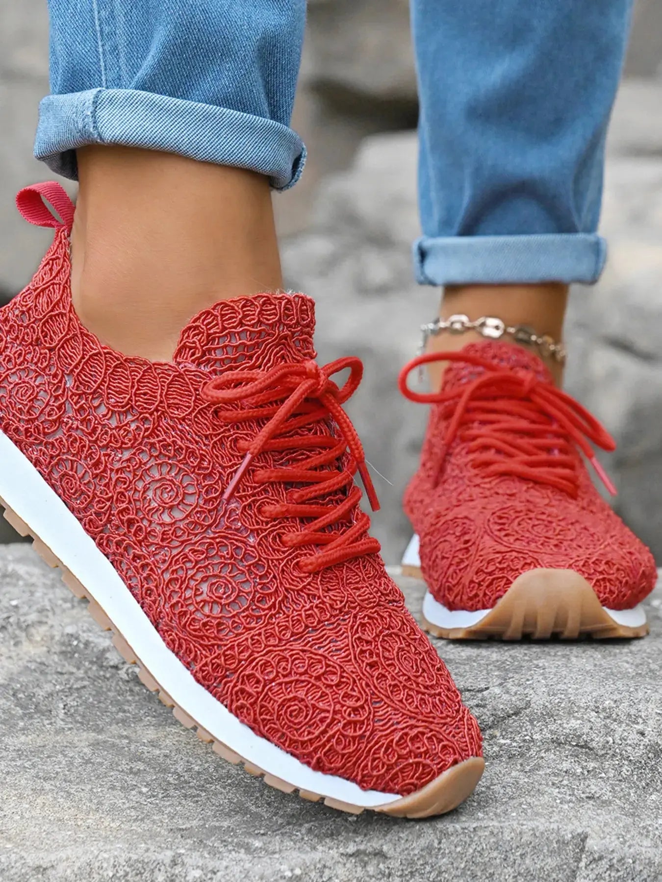 Red lace-up sneakers worn with rolled-up blue jeans on a concrete surface.