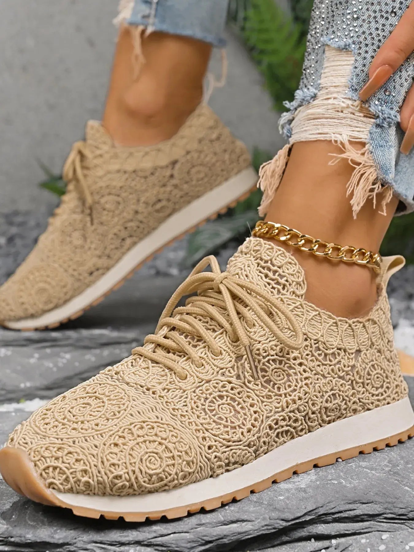 Beige crochet sneakers worn with rolled-up jeans on a gray surface.