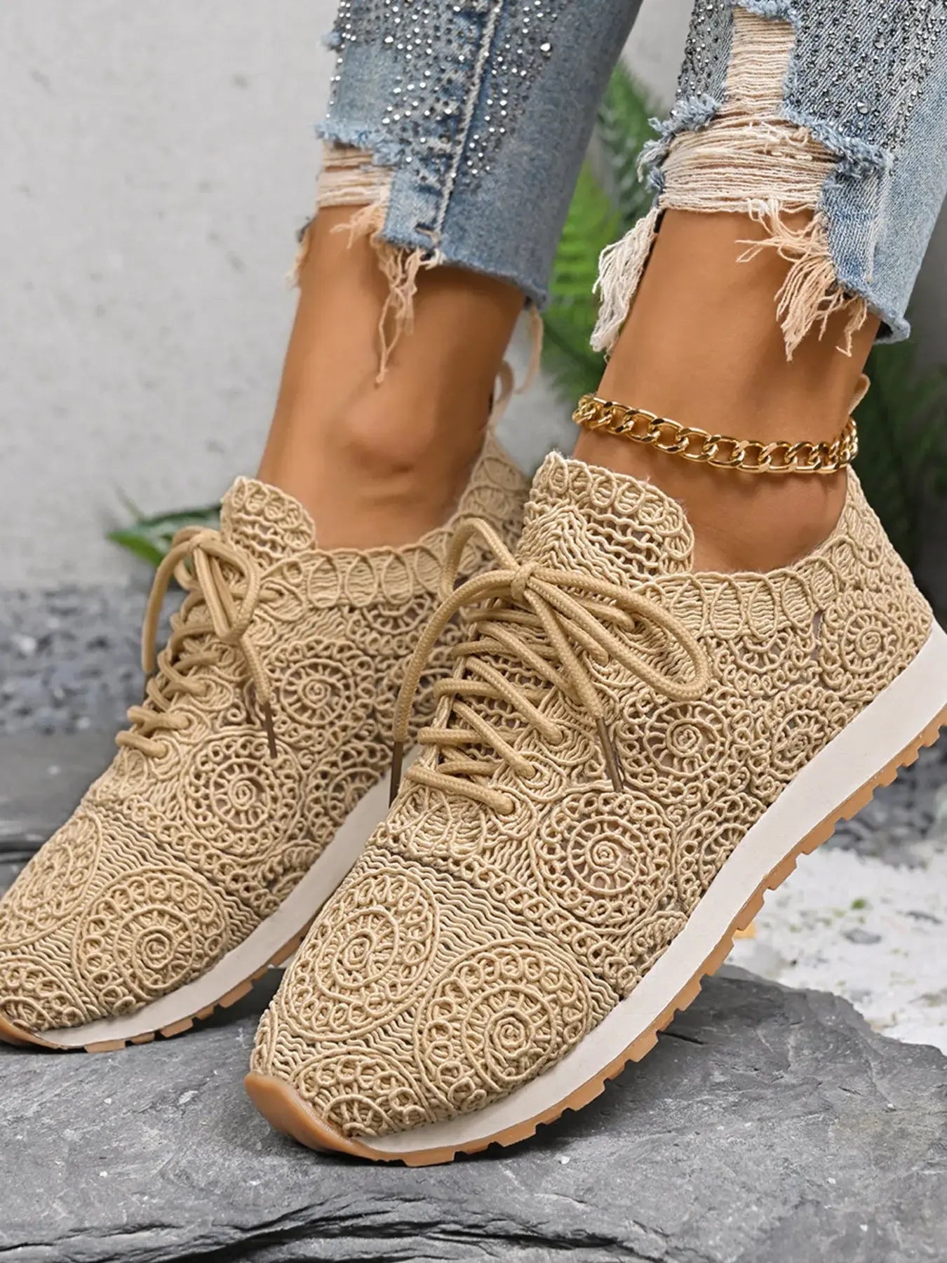 Beige lace-up sneakers worn with ripped jeans on a stone surface.