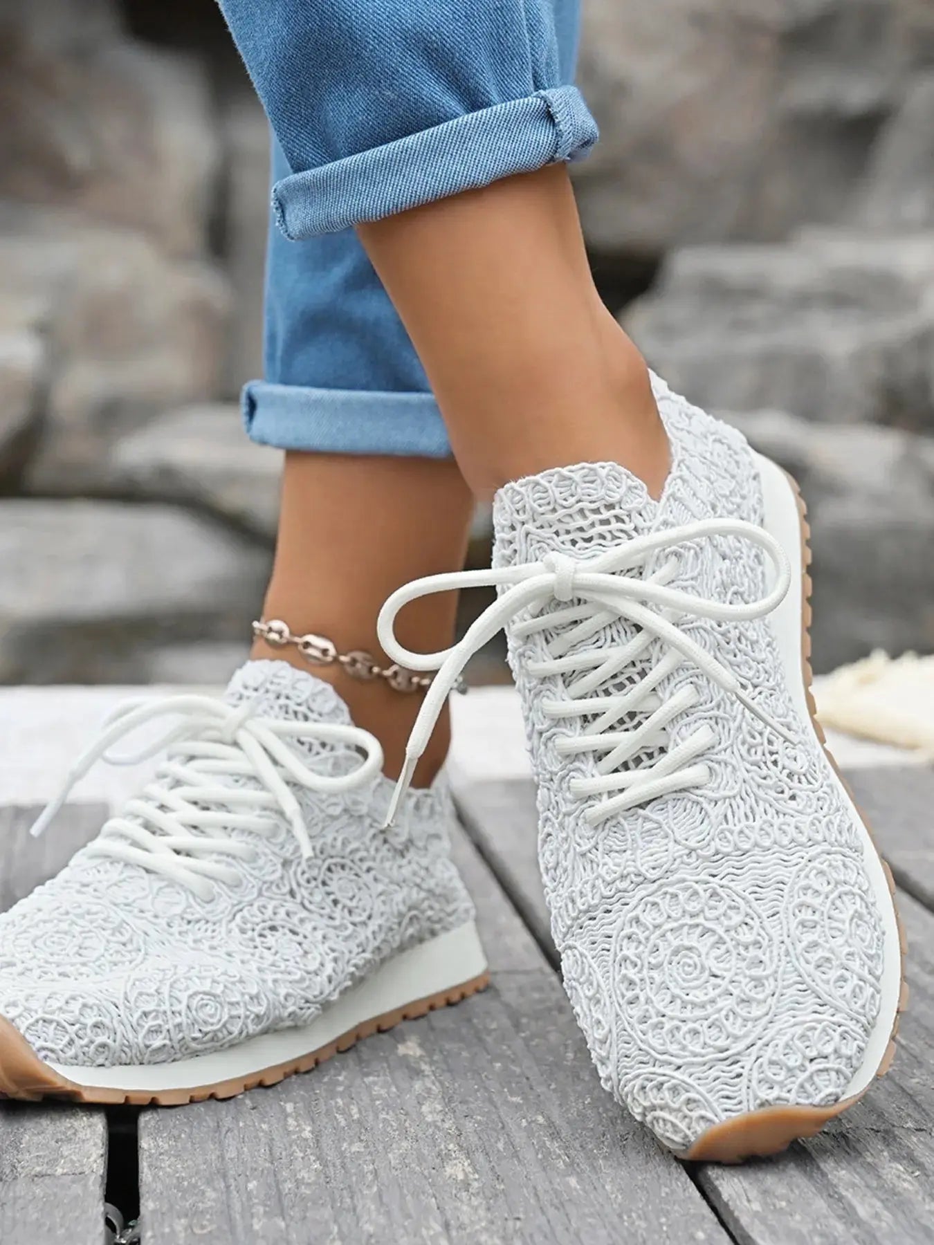 White textured sneakers worn with rolled-up jeans on a stone step.