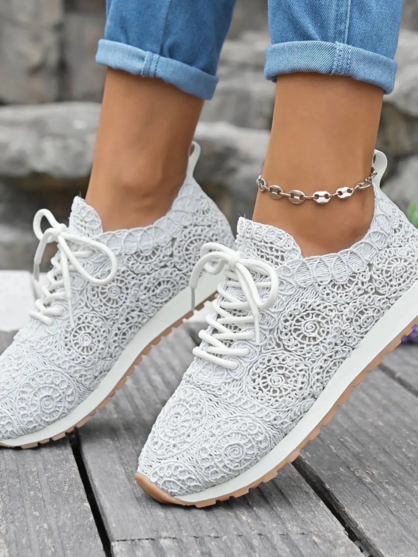 White lace-up sneakers worn with rolled-up jeans on a wooden surface.
