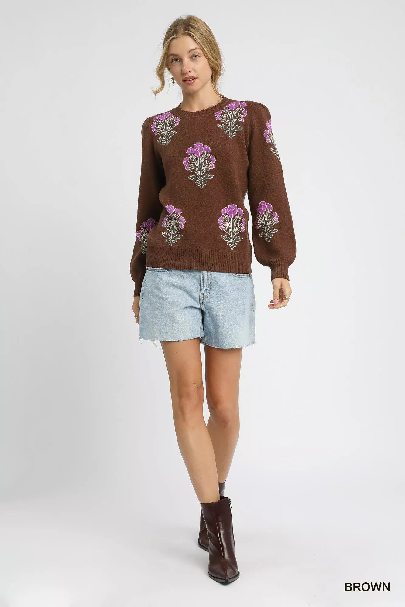 Woman wearing a brown sweater with floral patterns and light blue shorts on a white background