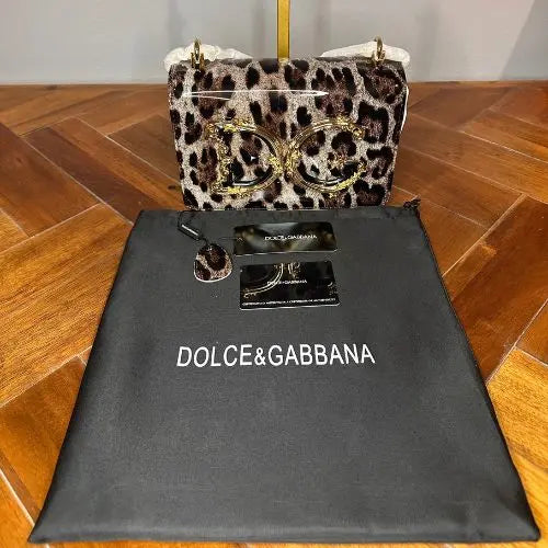 Leopard print handbag with gold accents on a Dolce & Gabbana branded black pouch.