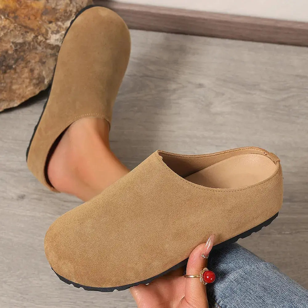 Brown slip-on shoe worn by a person on a wooden floor.
