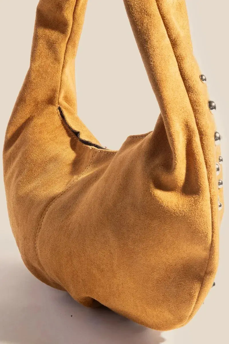 A camel-colored suede handbag with studded details on a light gray background.