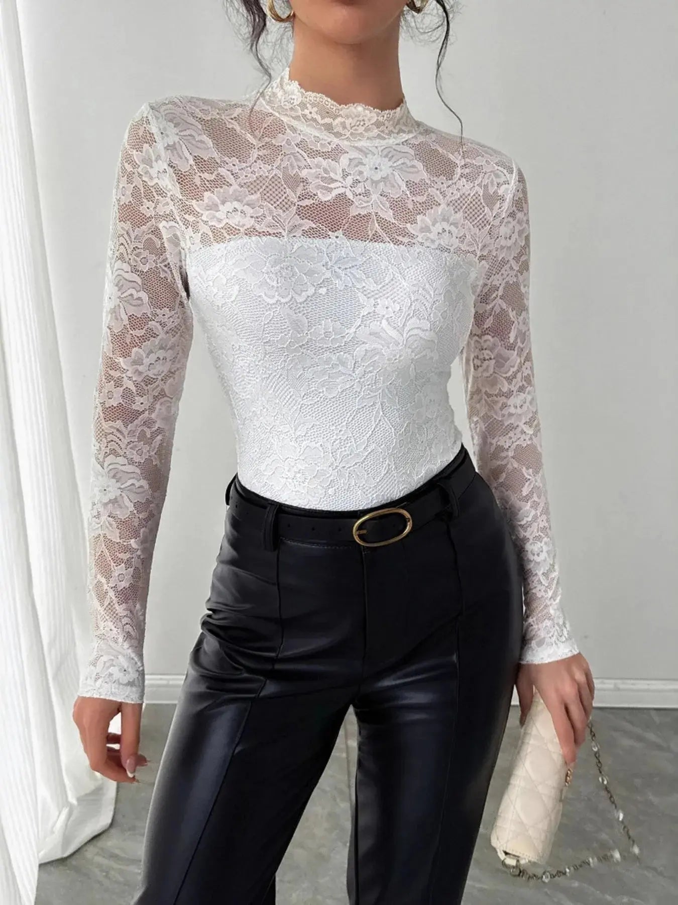 Person wearing a sheer lace top and black pants in a minimal indoor setting