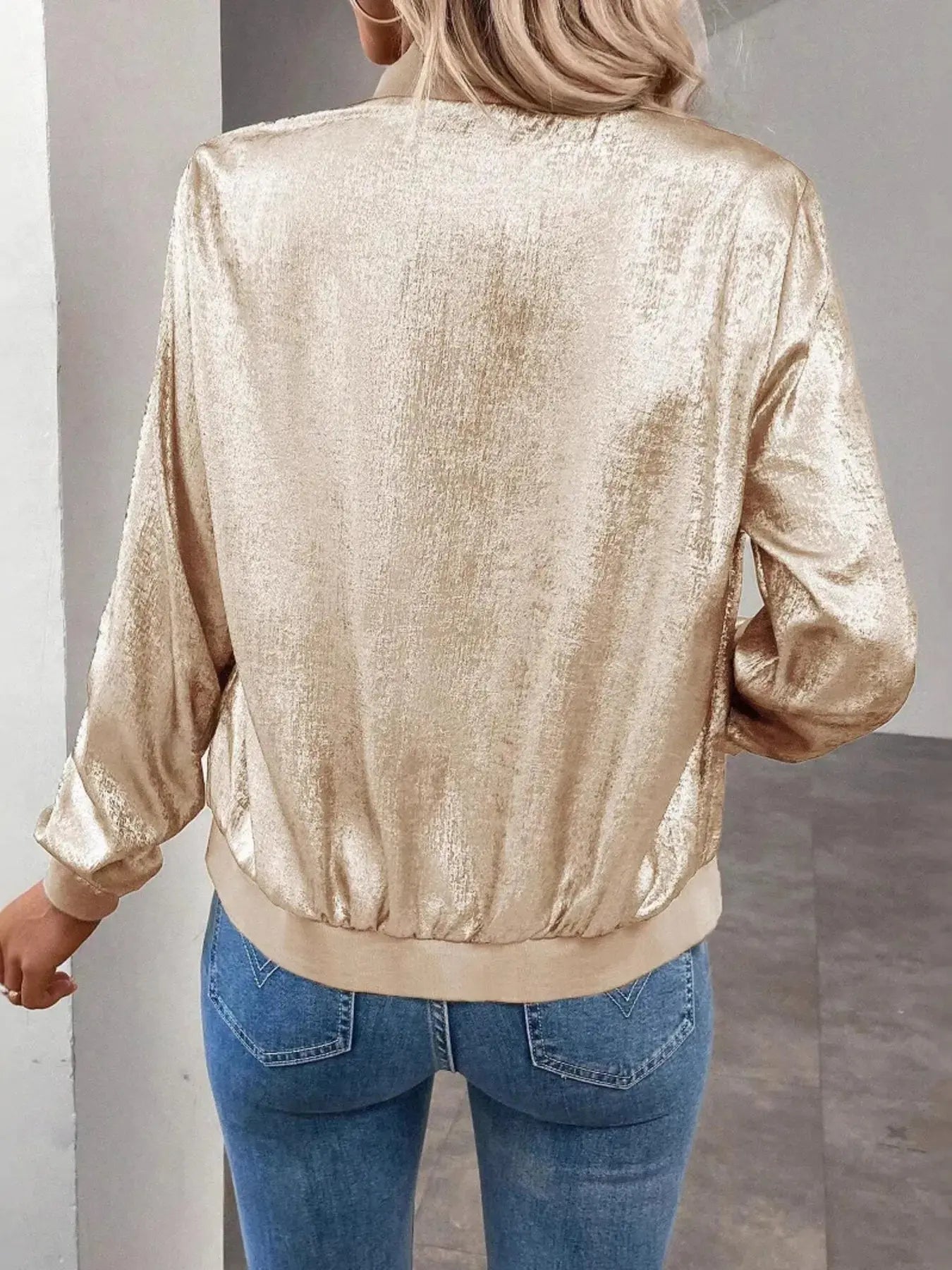 Person wearing a gold metallic jacket and blue jeans against a neutral background