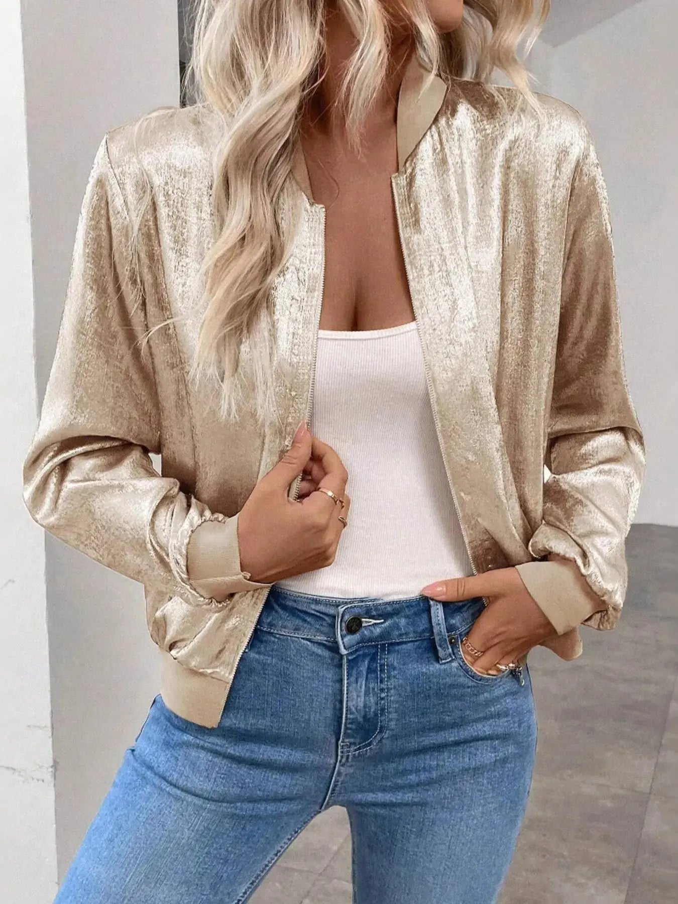 Person wearing a gold metallic jacket, white top, and blue jeans indoors.