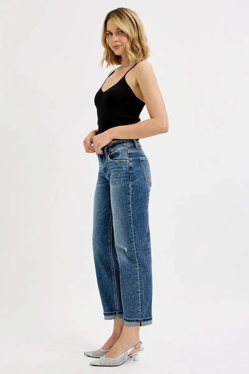 Woman standing to the side wearing a black top and blue jeans.