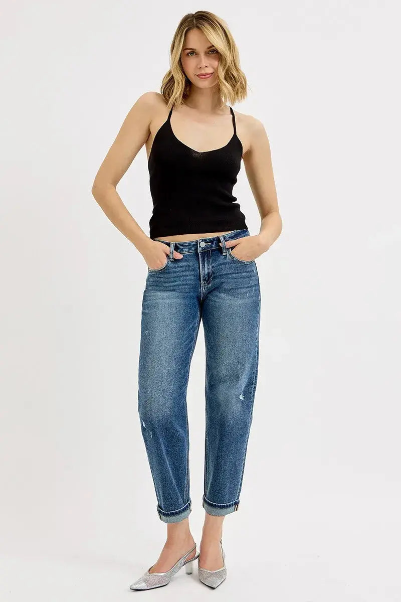 Woman wearing a black tank top and blue jeans on a white background.