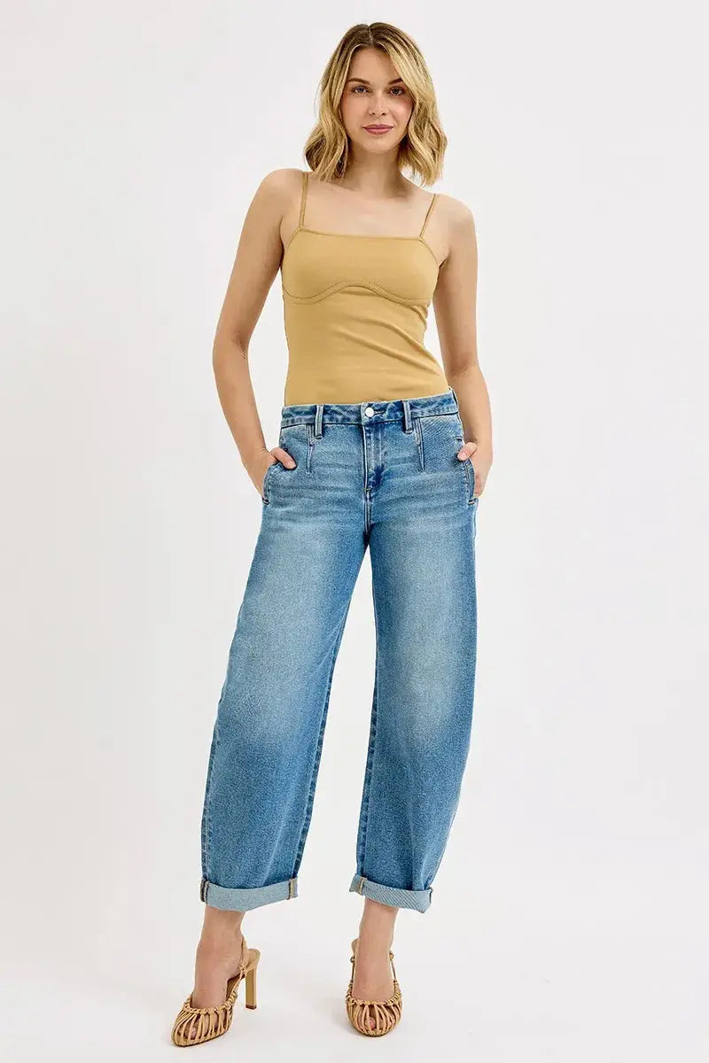 Woman wearing a beige tank top and rolled blue jeans on a white background