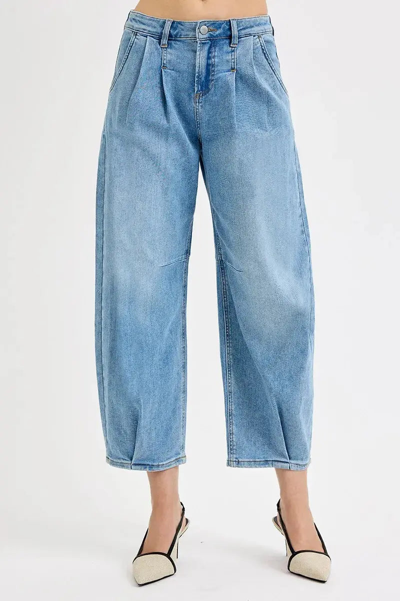 A person wearing light wash barrel style blue jeans on a white background.