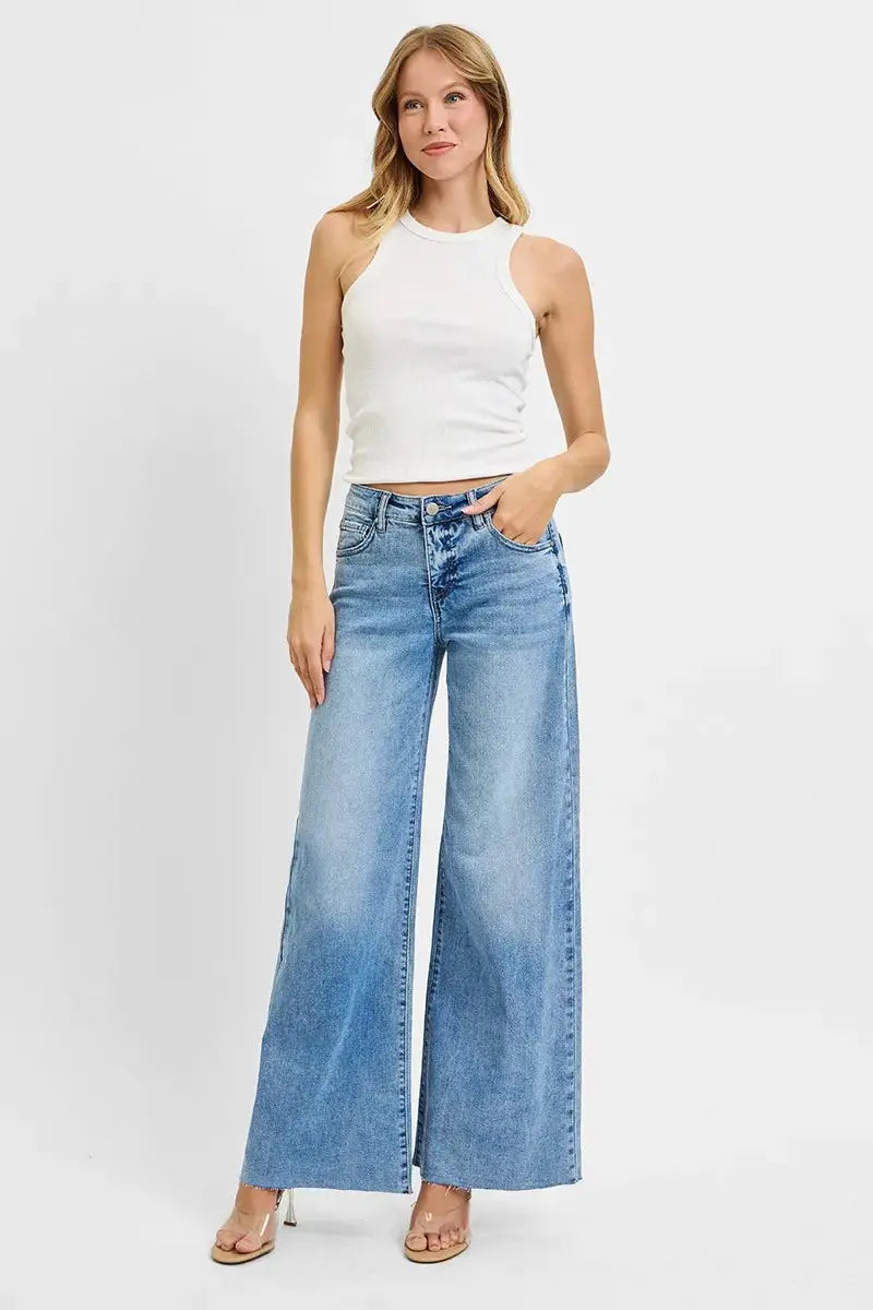 Woman wearing a white sleeveless top and blue wide-leg jeans on a white background