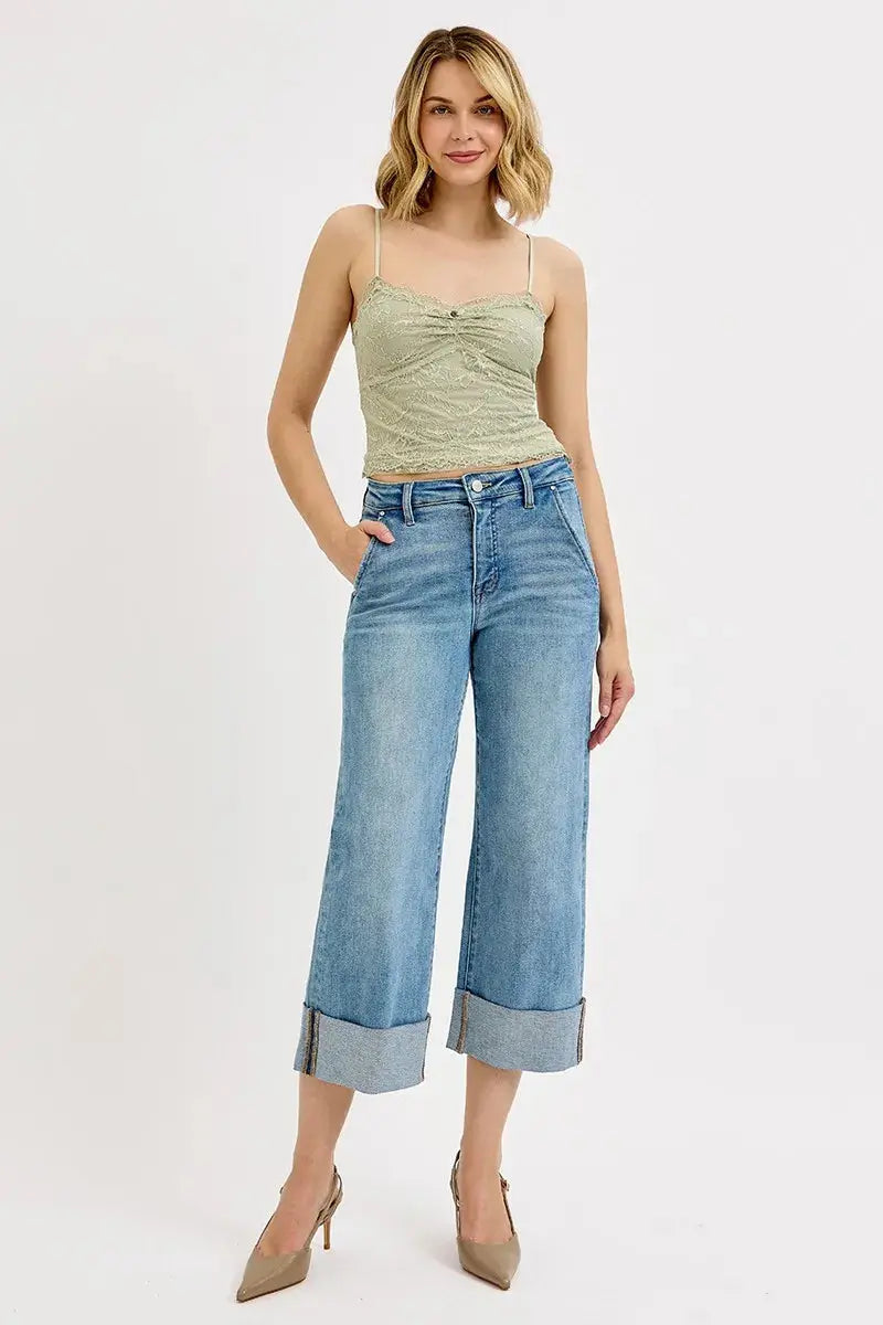 Woman wearing a beige tank top and cuffed light blue jeans on a white background