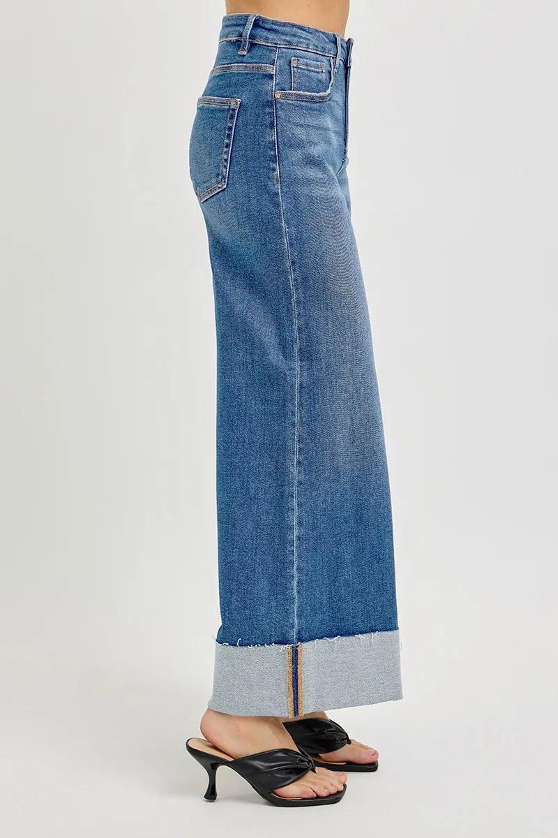 A side view of wide leg blue jeans with a cuffed hem on a white background