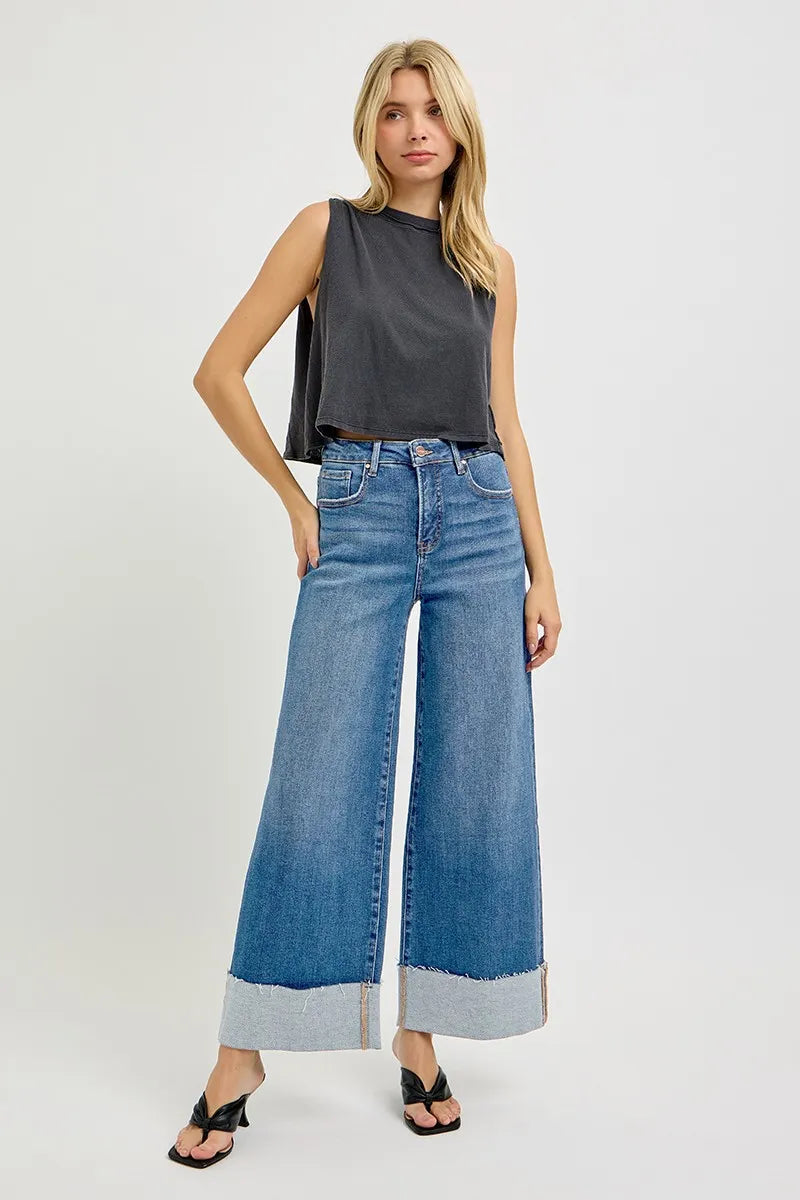 Woman wearing a sleeveless gray top and wide-leg blue jeans on a white background