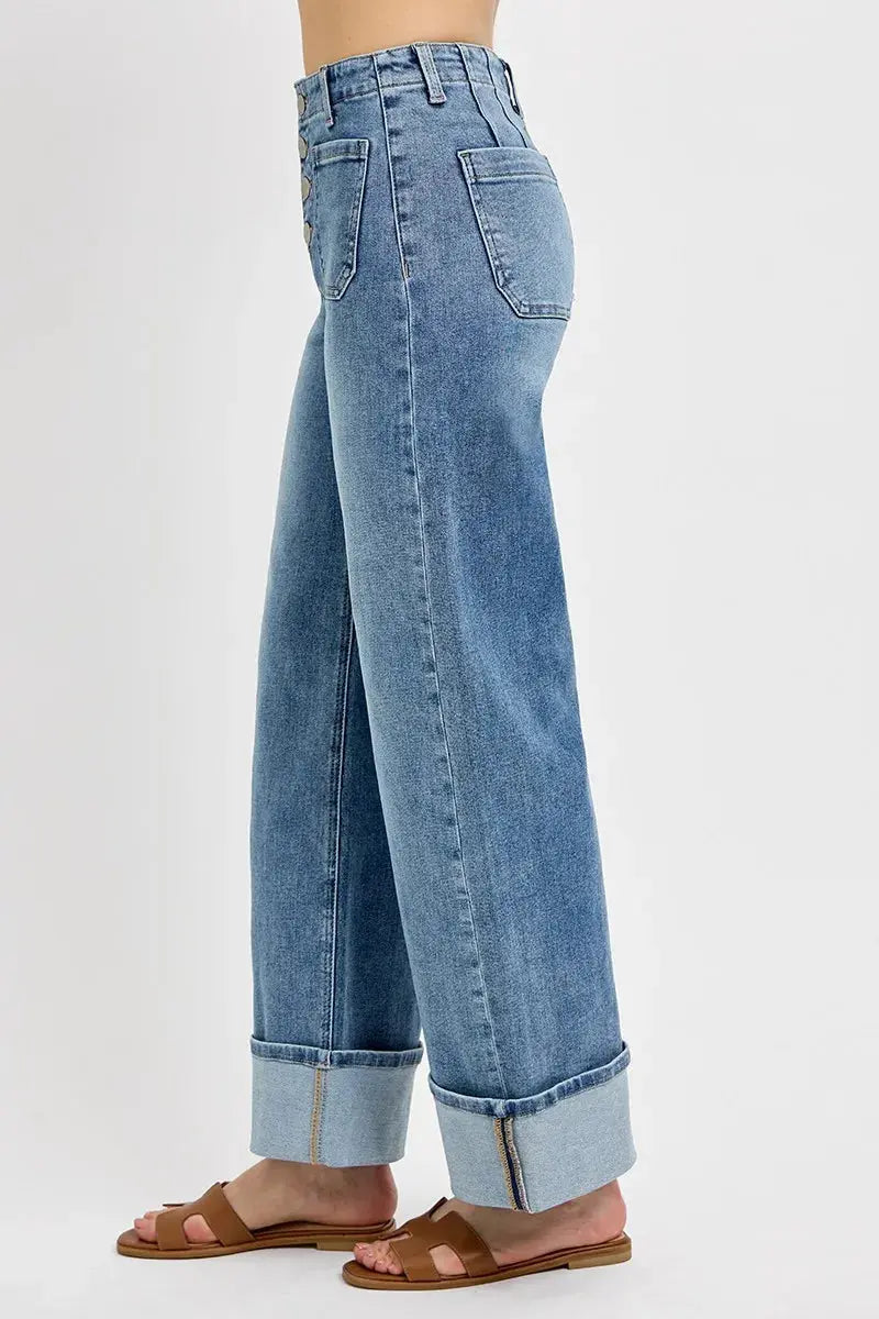 The side view of light blue wide leg jeans with large cuffs at the bottom are worn by a person on a white background