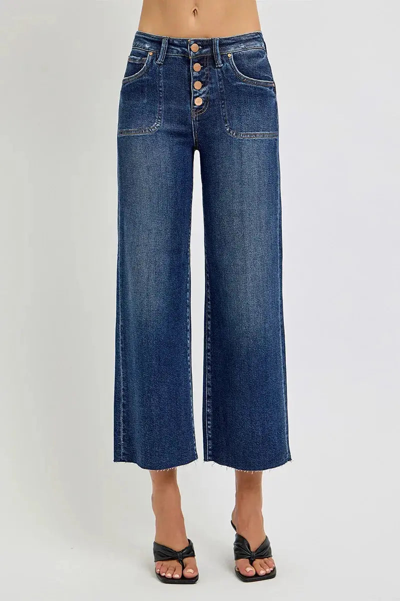 A person wearing blue jeans with a button fly on a white background.