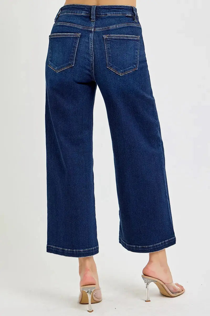 The back of wide leg dark washed blue jeans worn by a person on a white background