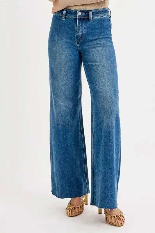 Blue jeans with wide legs and a raw hem worn by a person on a white background