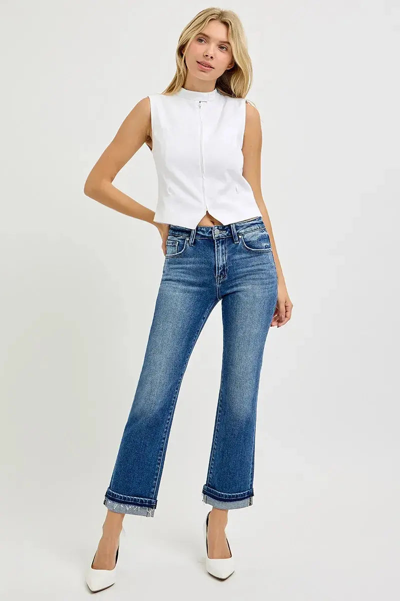 Woman wearing a white sleeveless blouse and cropped, cuffed blue jeans on a white background
