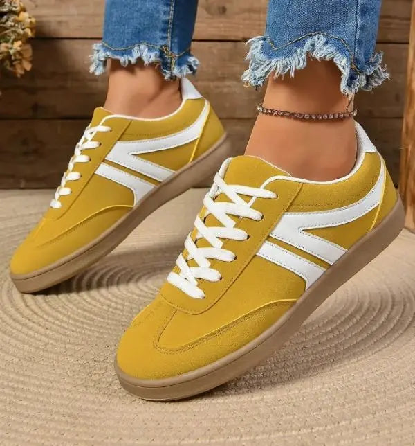 Yellow sneakers with white accents worn with blue jeans on a wooden floor.