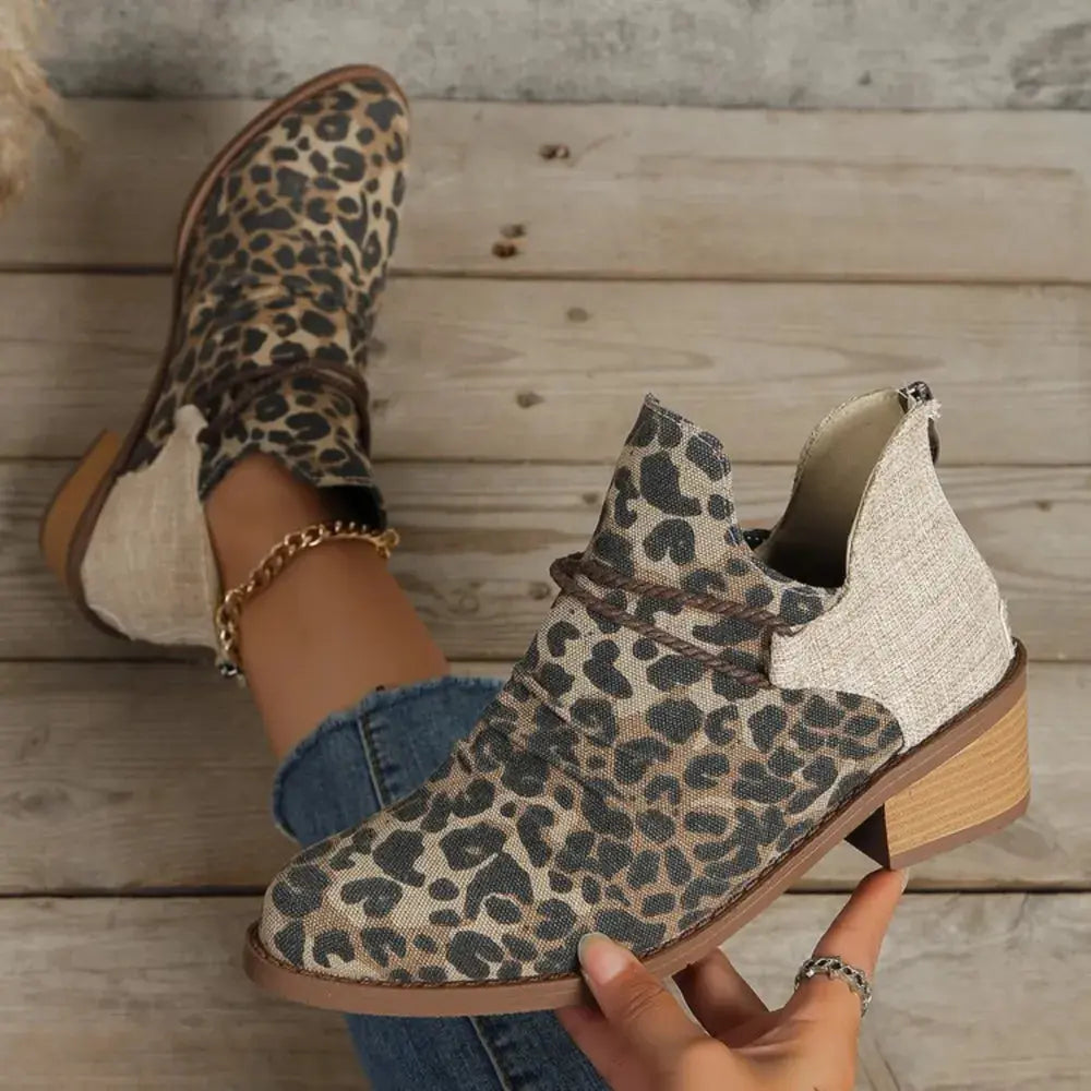 Leopard print ankle boots with wooden sole worn by a person on a wooden floor.