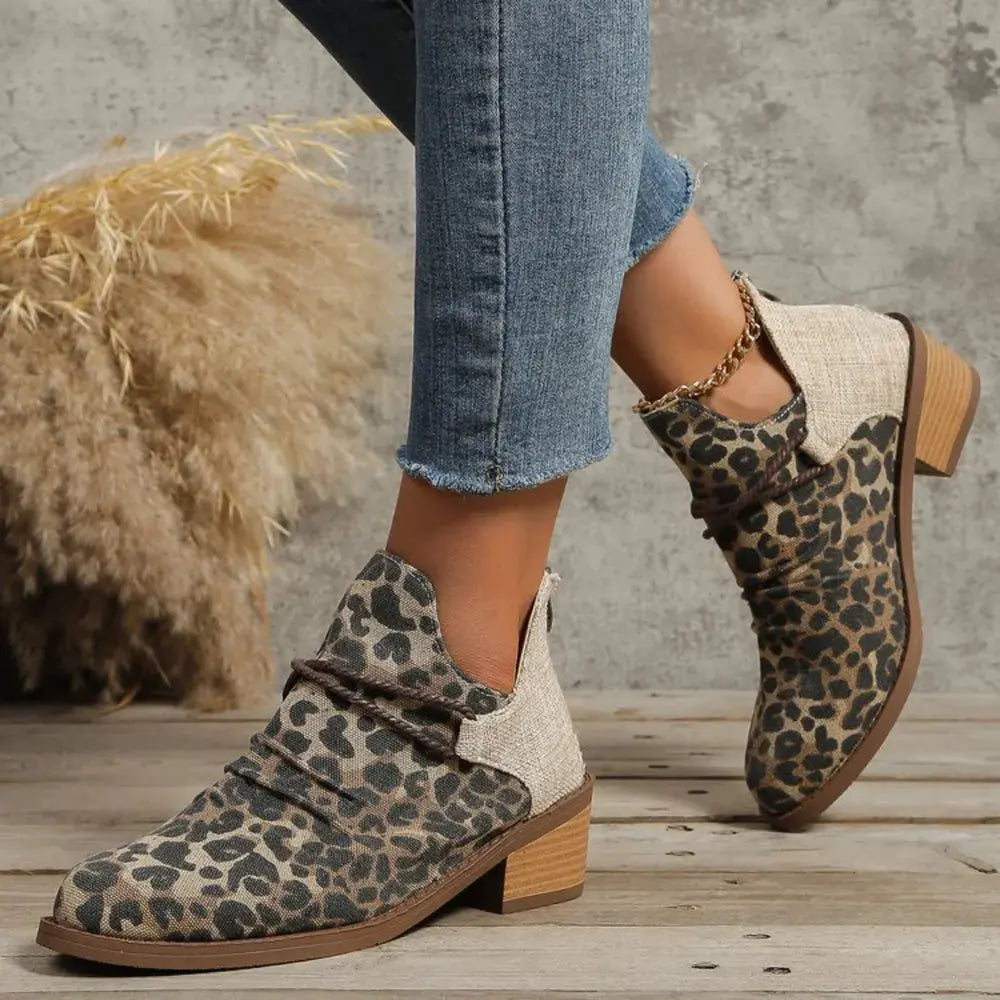 Leopard print ankle boots worn with jeans on a wooden floor.