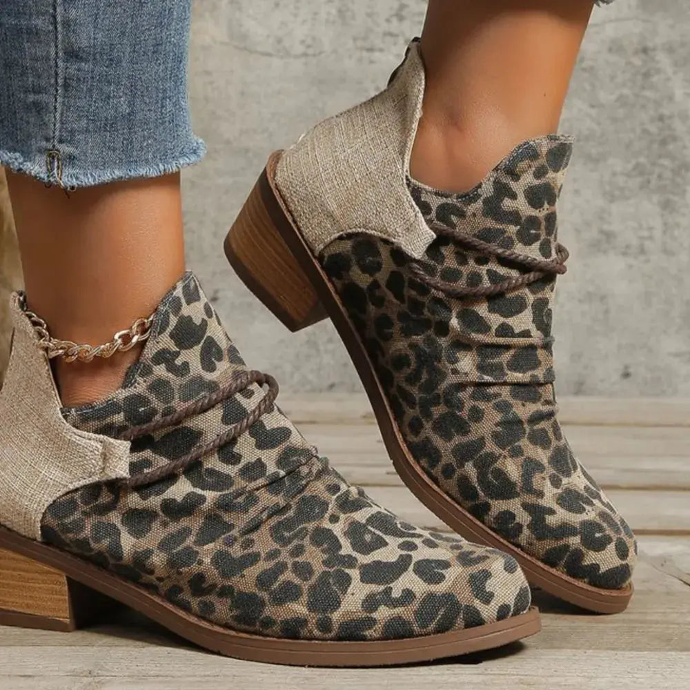 Leopard print boots worn with denim jeans on a wooden floor.