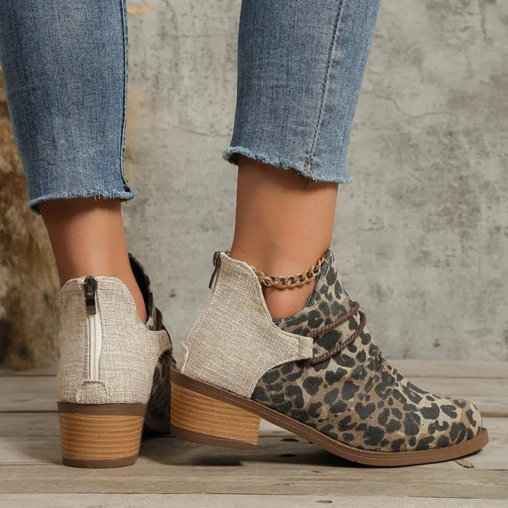 Leopard print ankle boots with beige fabric panels worn with blue jeans on a wooden floor.