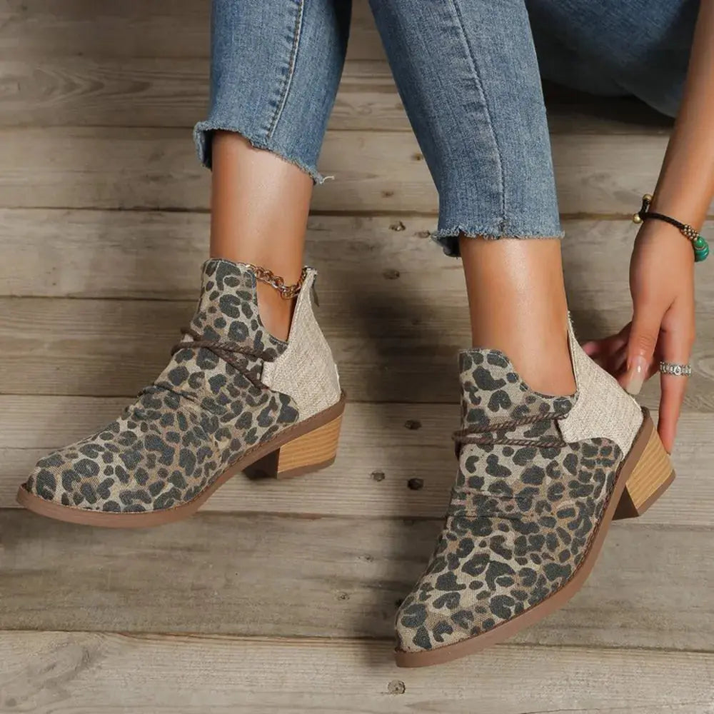 Leopard print ankle boots worn with jeans on a wooden floor.
