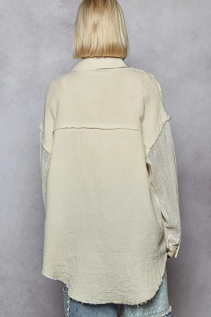 Person wearing a beige textured jacket with exposed seams and mesh sleeves is standing to show the back of the shirt.