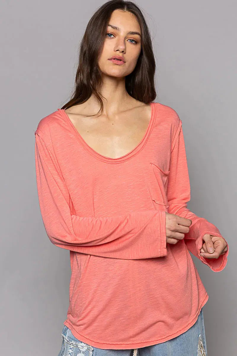 Woman wearing a coral-colored long-sleeve top against a gray background.