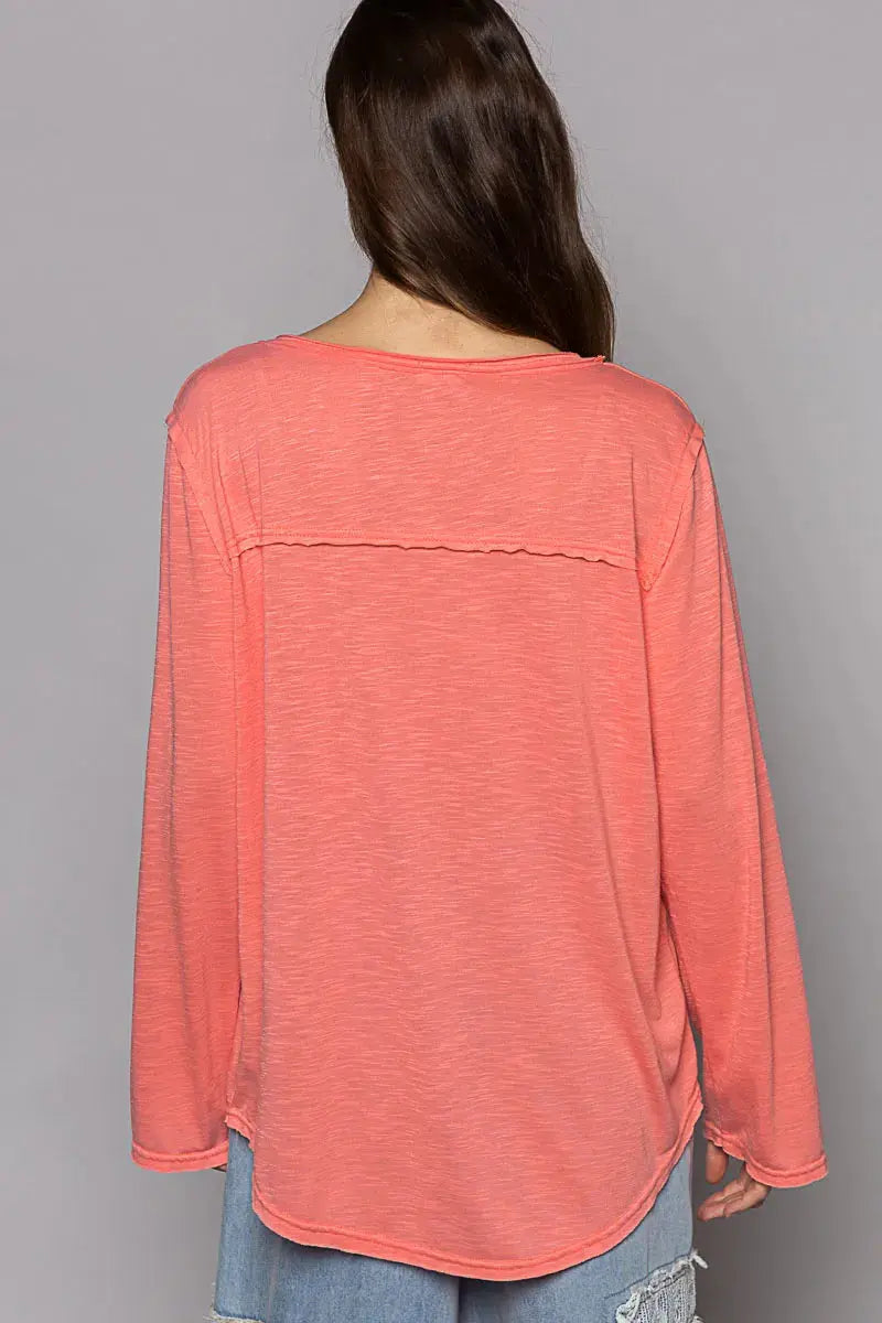 The back of a coral long-sleeve top worn by a person on a gray background.