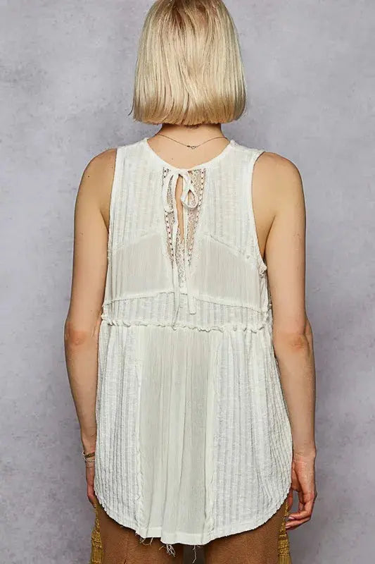 Person wearing a white sleeveless top with intricate detailing on a gray background.