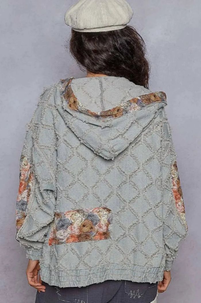 Person wearing a light blue quilted jacket with floral patterned patchwork on a gray background.