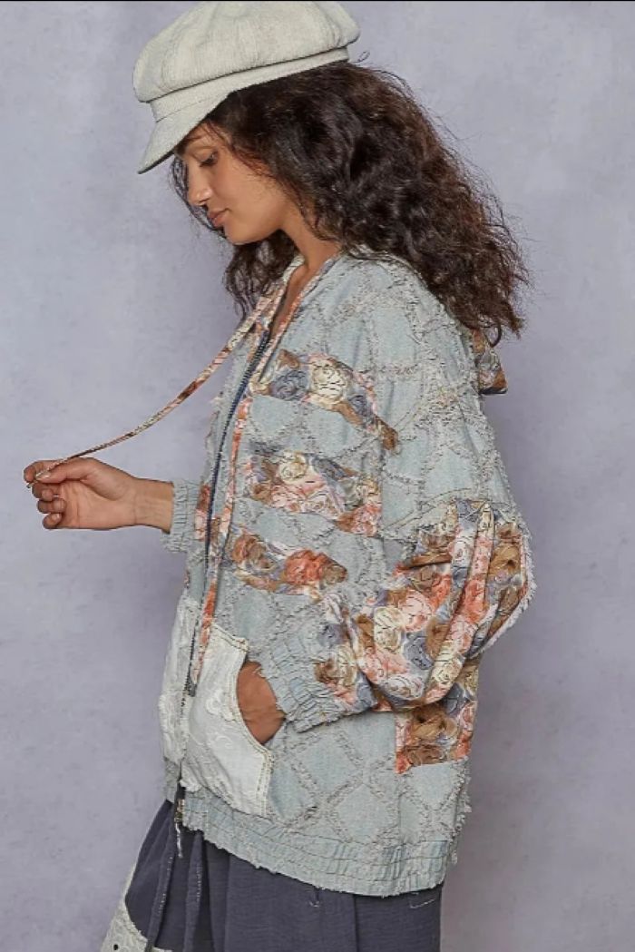 Woman standing to the side is wearing a denim jacket that zips up and has floral embellishments.