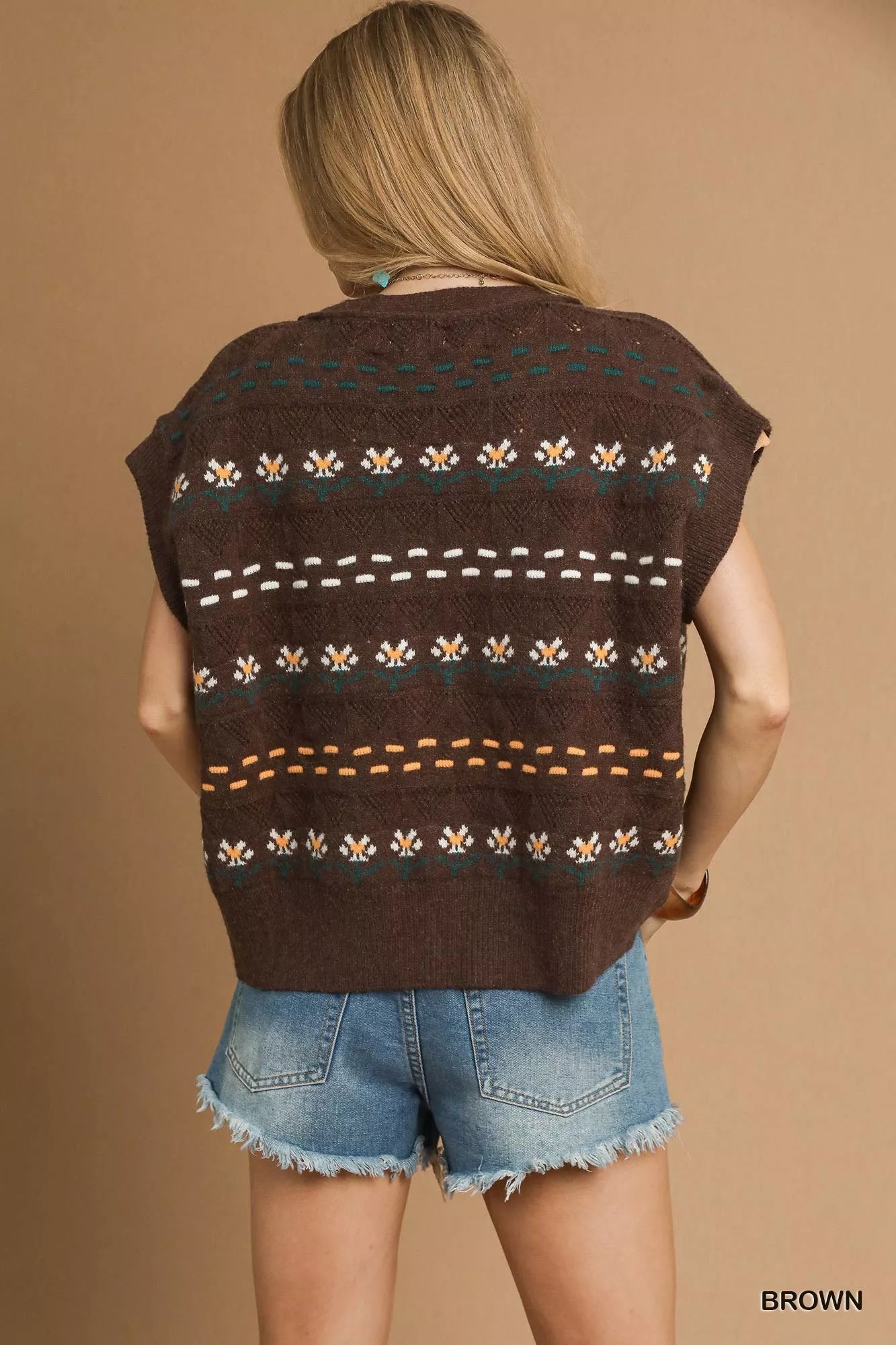 Person wearing a brown patterned vest over denim shorts on a beige background