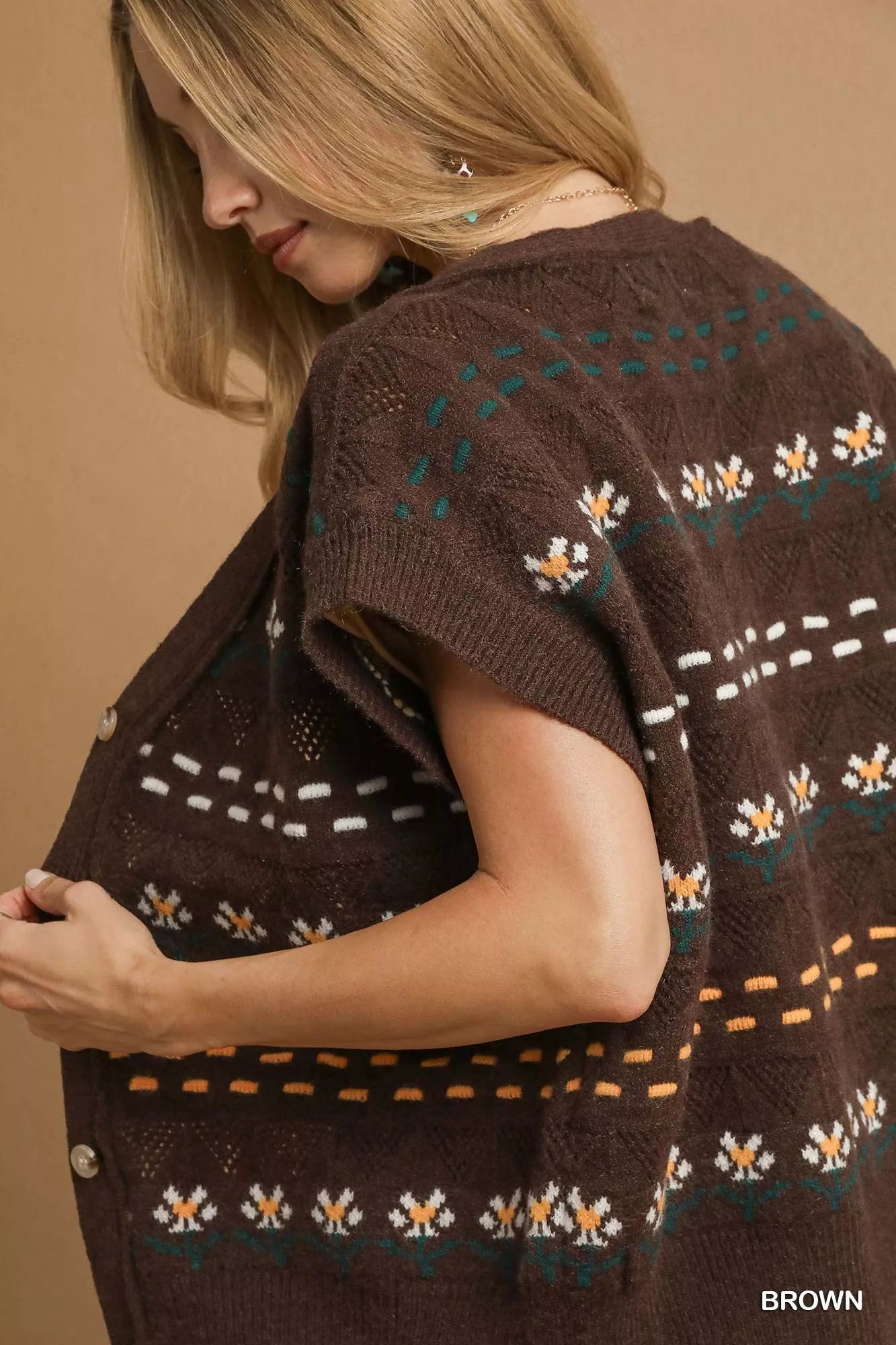 Woman wearing a brown knitted cardigan with floral patterns on a beige background