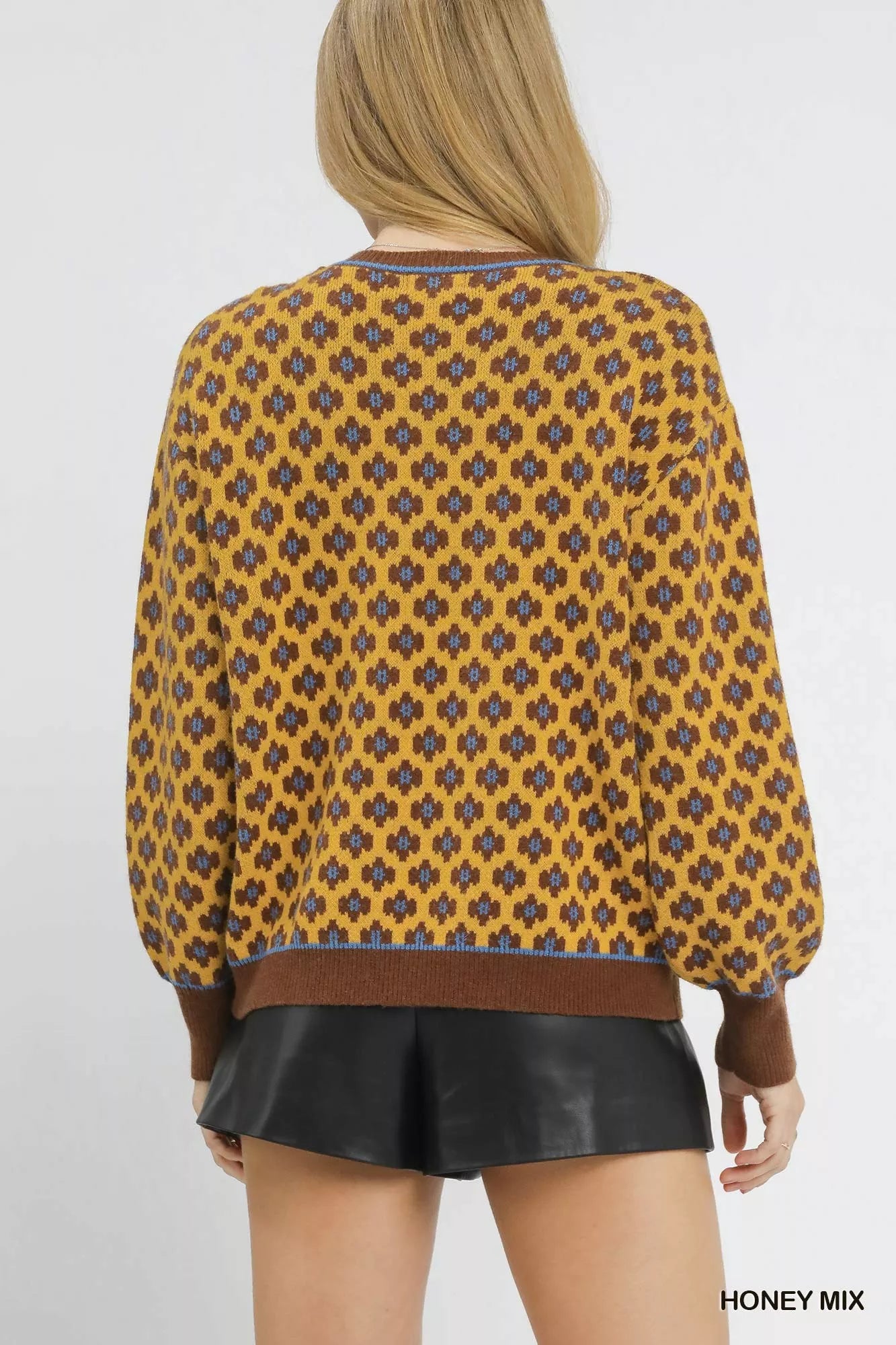 Person wearing a patterned yellow and brown sweater with leather shorts on a white background