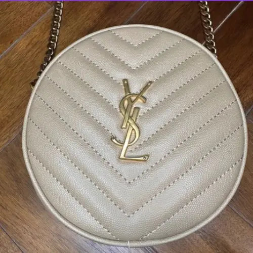 Round quilted handbag with a gold logo on a wooden floor