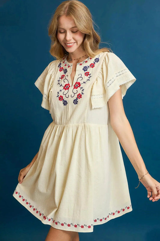 This charming bohemian-style mini dress features beautiful multicolored floral embroidery across the chest and hem, creating an eye-catching focal point. Made from lightweight cotton blend fabric, it offers comfort and breathability. The flutter sleeves add a romantic touch while the elastic waist ensures a flattering fit. 
