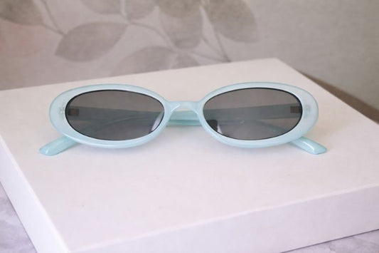 Light Blue 90s style sunglasses on white stand and neutral background