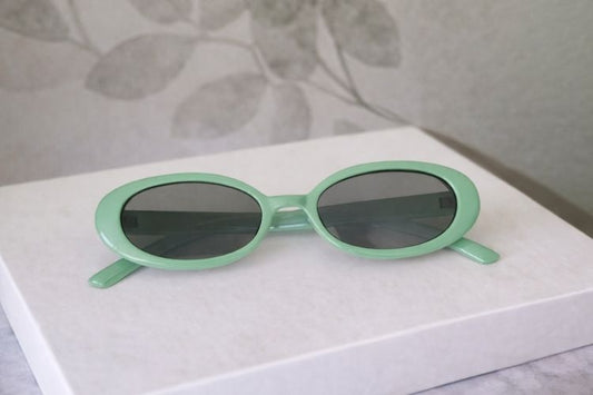 Green sunglasses on a white surface with a floral-patterned background