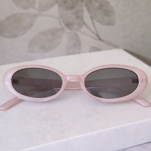 Pink sunglasses with dark lenses on a light surface