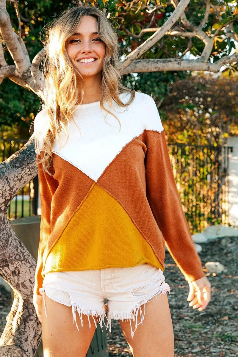 Woman wearing a colorful sweater and shorts standing outdoors near trees.